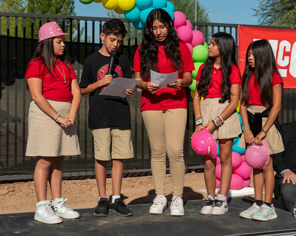 Galveston students stand on stage. Some are wearing colorful plastic construction hats